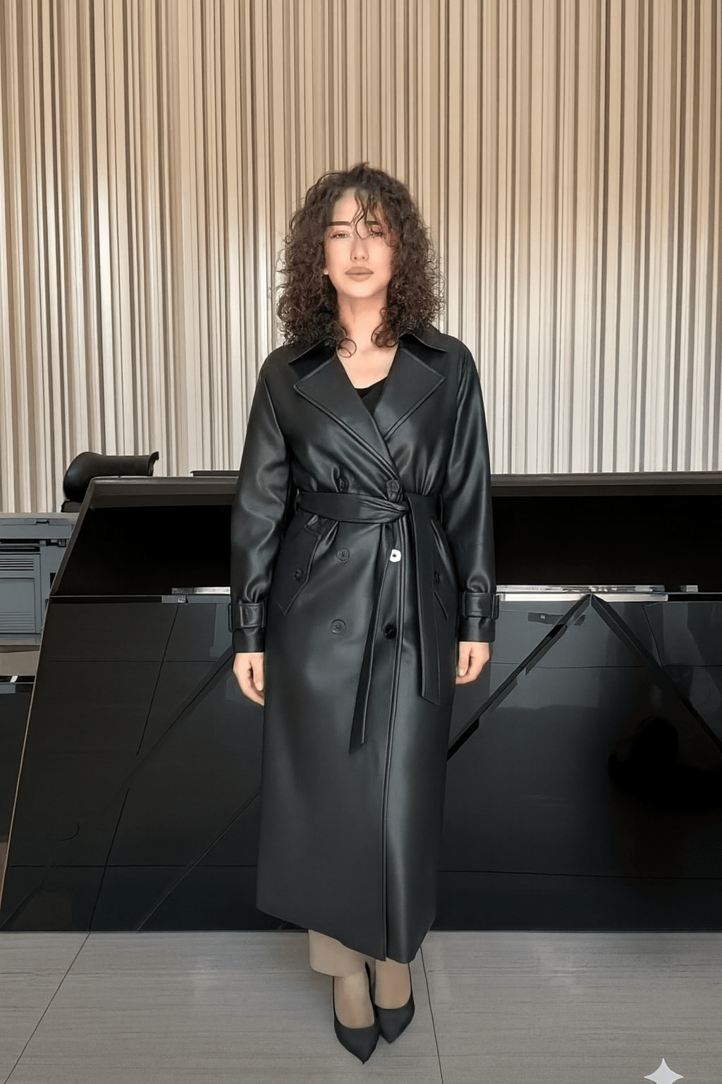 Woman wearing a black leather trench coat in an indoor setting